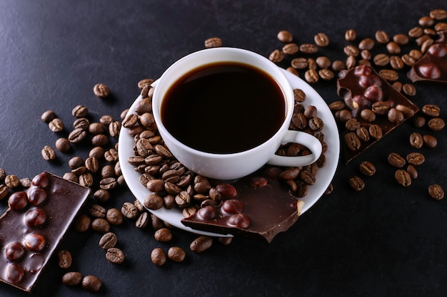 Granos de café dispersos, una taza y chocolate negro sobre una mesa de piedra negra. Copia espacio