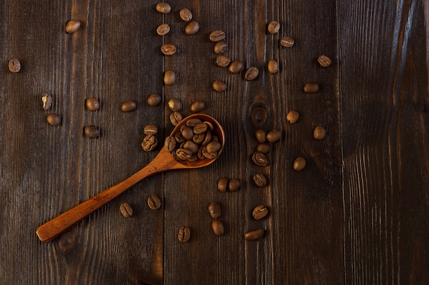 Granos de café esparcidos sobre un fondo de madera oscura con una cuchara de madera