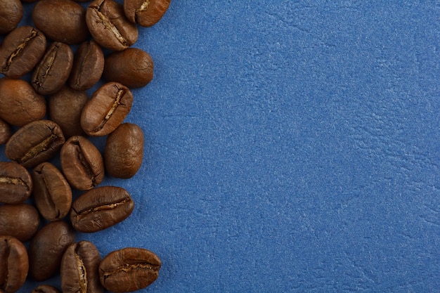 Los granos de café están esparcidos sobre un fondo azul desde el borde del marco Café sobre un fondo azul