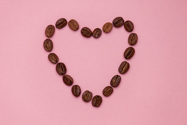 Granos de café en forma del corazón en fondo rosado. Copia spase