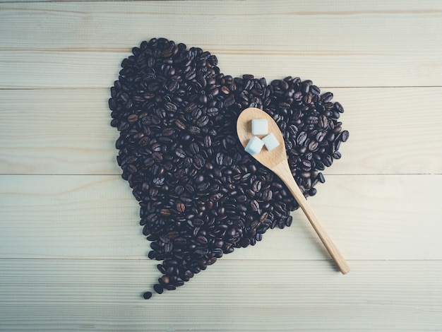 Granos de café en forma de corazón sobre fondo de madera con cuchara de madera y azúcar