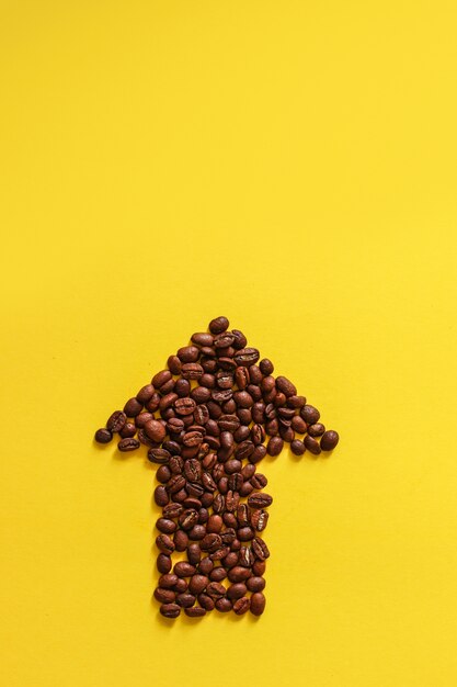 Foto granos de café bajo la forma de flechas aisladas en fondo amarillo.