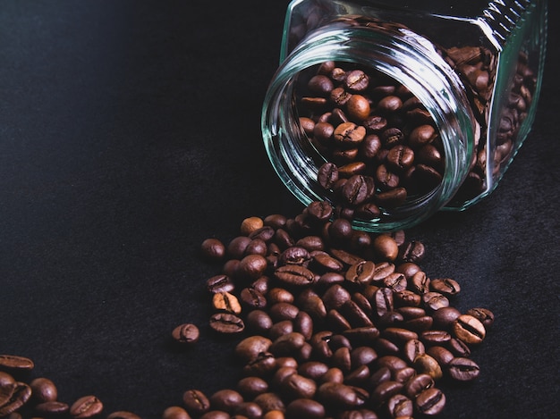 Foto granos de café de un frasco de vidrio sobre un fondo negro