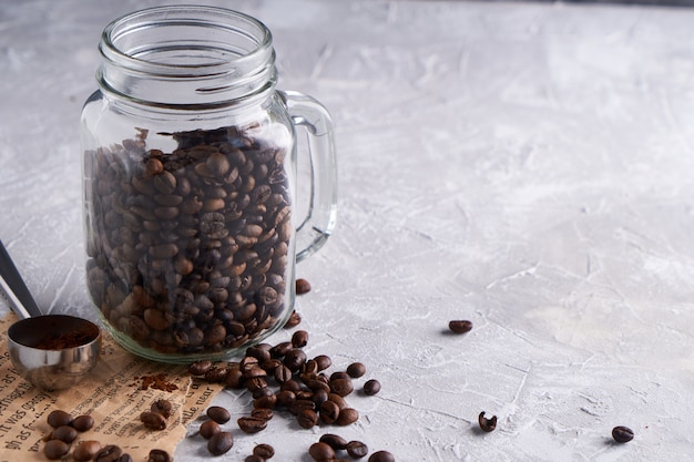 Granos de café en un frasco de vidrio sobre una mesa gris