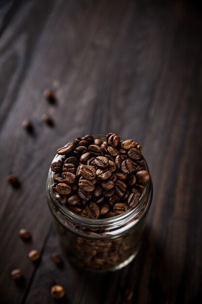 Granos de café en frasco de vidrio sobre mesa de madera