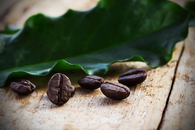 Granos de café y hoja verde sobre fondo de madera