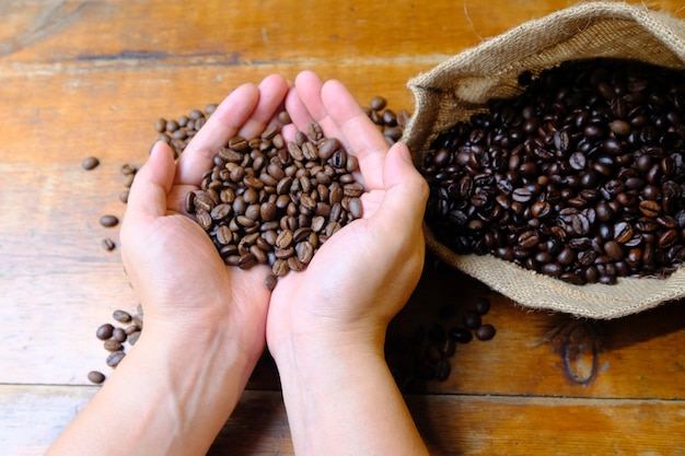 Granos de café en las manos con una bolsa de café y una taza de café con leche