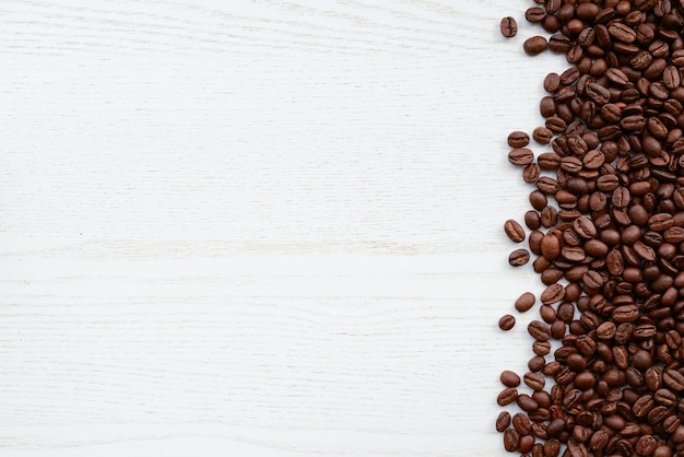 Granos de café en una mesa de madera blanca Granos de café tostados en una vista superior de fondo de madera blanca