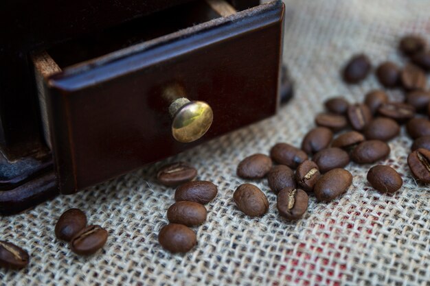 Granos de café con un molinillo de café de madera sobre una arpillera. Preparación de una bebida aromática. De cerca.