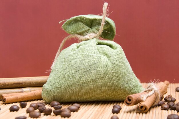 Granos de café y palitos de canela en saco de lona sobre fondo de madera Bolsa verde