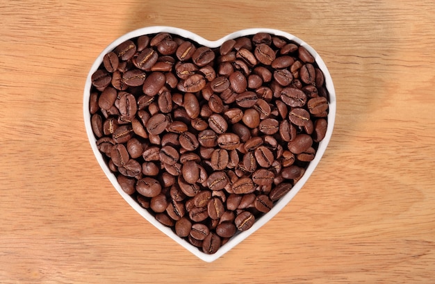 Granos de café en placa en forma de corazón en un fondo de madera