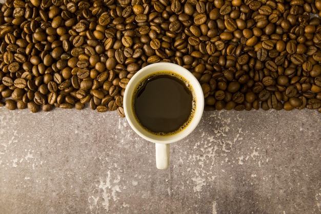 Granos de café sobre un fondo negro con una taza blanca