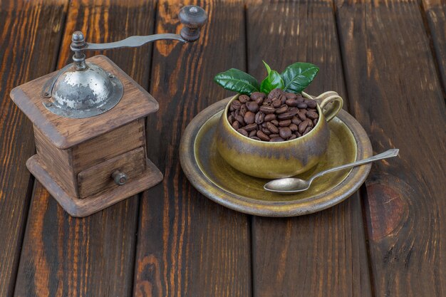 Granos de café en una taza y antiguo molinillo de café manual sobre una mesa de madera