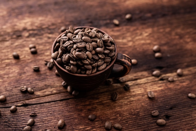Granos de café en una taza de arcilla sobre un fondo antiguo de madera marrón.