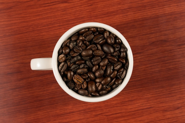 Granos de café en una taza blanca con fondo de madera