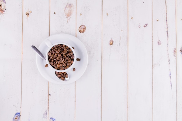 Granos de café en una taza blanca sobre una mesa de madera