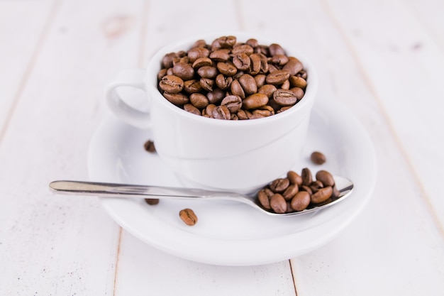 Granos de café en una taza blanca sobre una mesa de madera