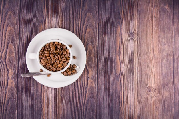 Granos de café en una taza blanca sobre una mesa de madera