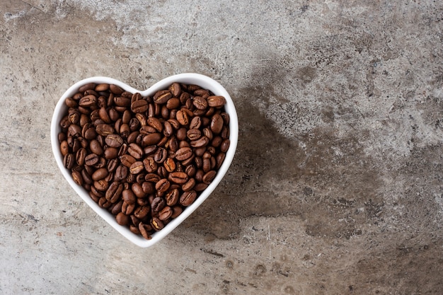 Granos de café en una taza de corazón sobre un fondo de hormigón