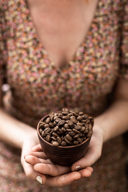 Granos de café en una taza en manos femeninas sobre un fondo marrón.