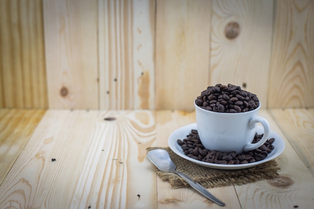 Granos de café en taza sobre fondo de madera