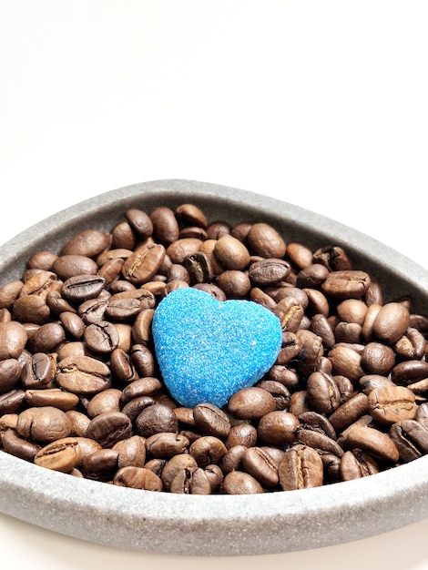 Granos de café en un tazón y corazón de mermelada sobre un fondo blanco.