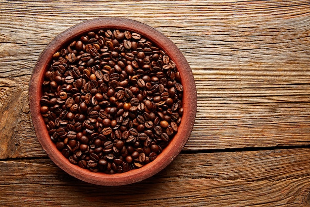 Granos de café en una textura de plato de arcilla en la madera