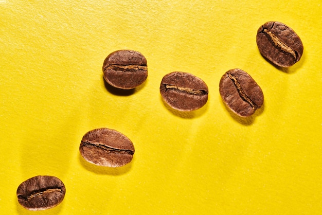 Granos de café tostados aislados de cerca en el camino de recorte de fondo amarillo