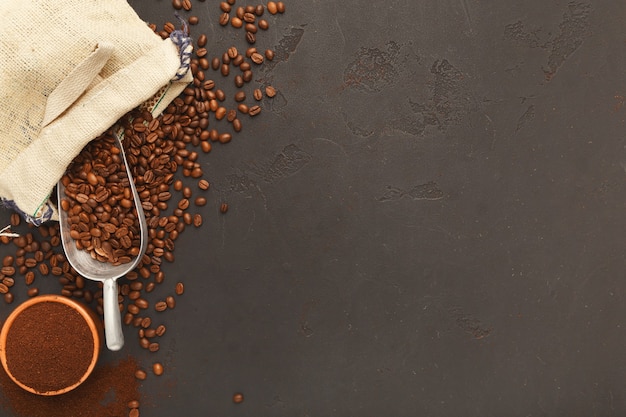 Granos de café tostados en bolsa de arpillera y cuchara vieja sobre fondo de textura gris con espacio de copia. Diseño minimalista para publicidad de cafetería, vista superior.