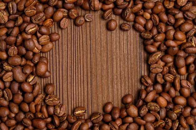 Los granos de café tostados crean un círculo para copiar el espacio en el fondo de madera quemada.