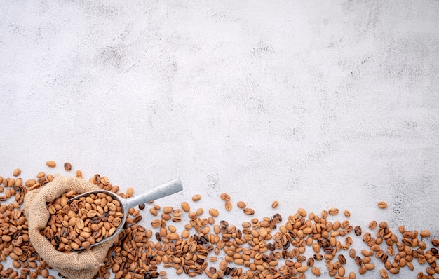 Granos de café tostados con cucharadas sobre hormigón blanco.