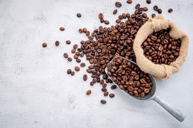 Granos de café tostados con cucharadas sobre hormigón blanco.