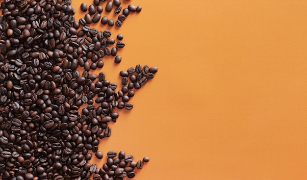 Granos de café tostados en fondo naranja vista superior Pila de mitades de granos de café marrón oscuro