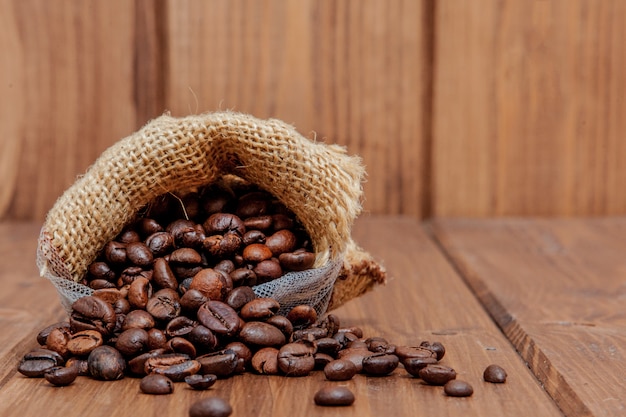 Granos de café tostados frescos cayendo el saco en la superficie de madera.