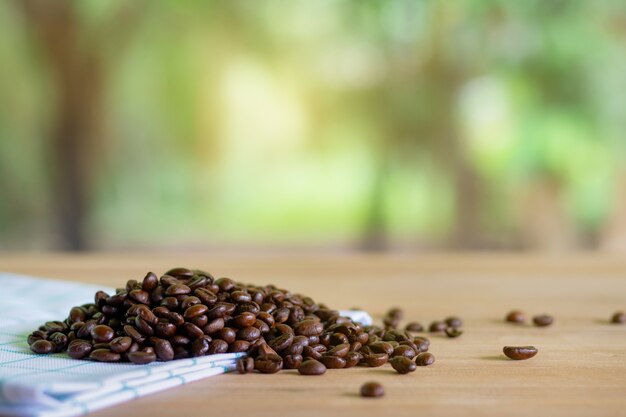 Granos de café tostados en madera con el fondo de la naturaleza.