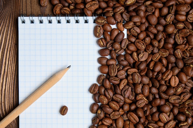 Granos de café tostados con papel de bloc de notas y lápiz de fondo