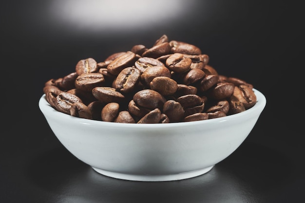 Granos de café tostados en un recipiente aislado de cerca en el camino de recorte de fondo negro