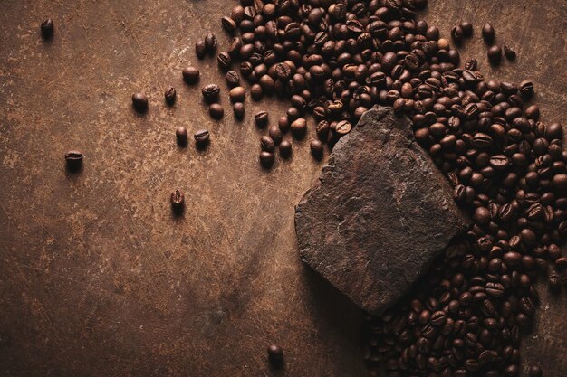 Granos de café tostados sobre pedestal de piedra fondo marrón