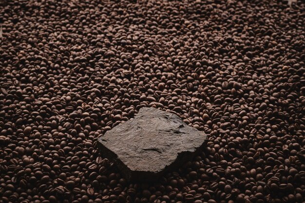 Foto granos de café tostados sobre pedestal de piedra fondo marrón