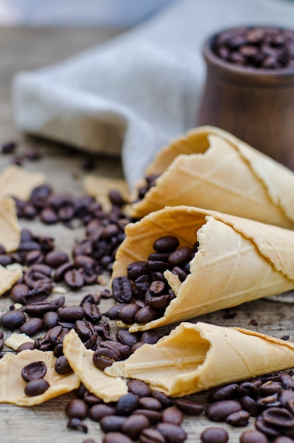 Granos de café tostados en una taza de cerámica y conos de gofres de azúcar