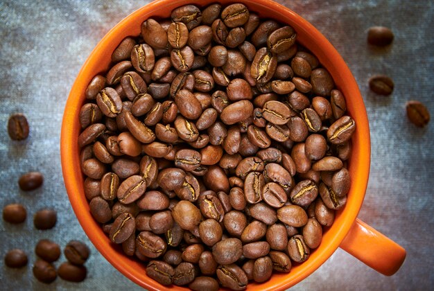 Granos de café tostados en una taza de naranja sobre un fondo plateado