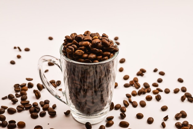 Los granos de café se vierten en una taza de vidrio sobre un fondo blanco.