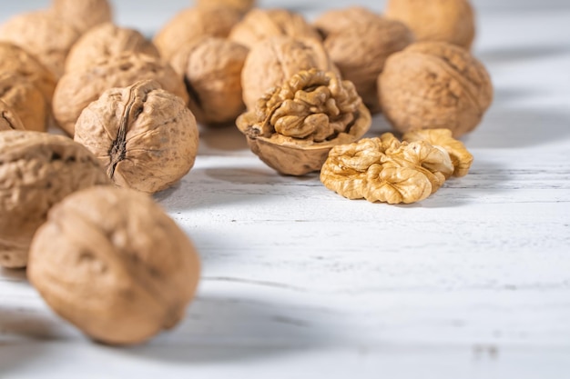 Foto granos de nueces en el escritorio de madera blanca con lugar para el texto. montón de cáscaras de nueces enteras