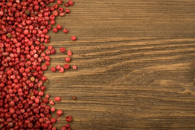 Granos de pimienta rosa o pimiento rojo sobre mesa de madera. Semillas secas de Schinus