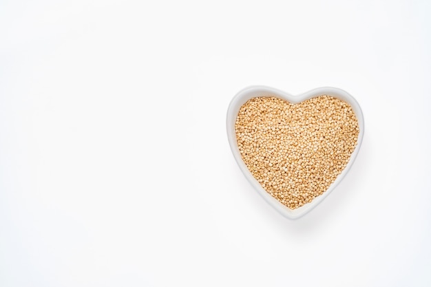 Granos de quinua en un recipiente con forma de corazón aislado en el cuadro blanco, vista superior