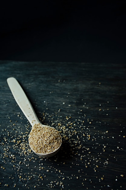 Foto granos de trigo en una cuchara de madera sobre un fondo oscuro de madera.