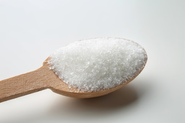 Granulierter Zucker im Holzlöffel auf weißem Hintergrund