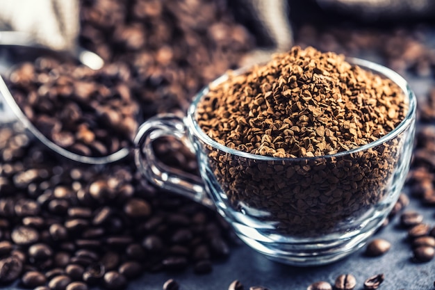 Gránulos de café instantáneo en taza de vidrio y granos de café.