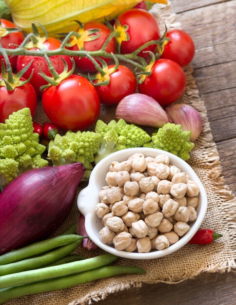 Grão de bico em uma tigela com vegetais crus, close-up em uma mesa de madeira