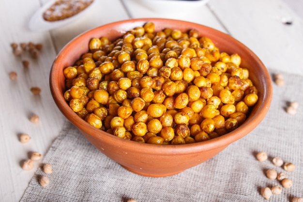 Grão de bico frito com especiarias em um prato de barro na superfície de madeira branca.